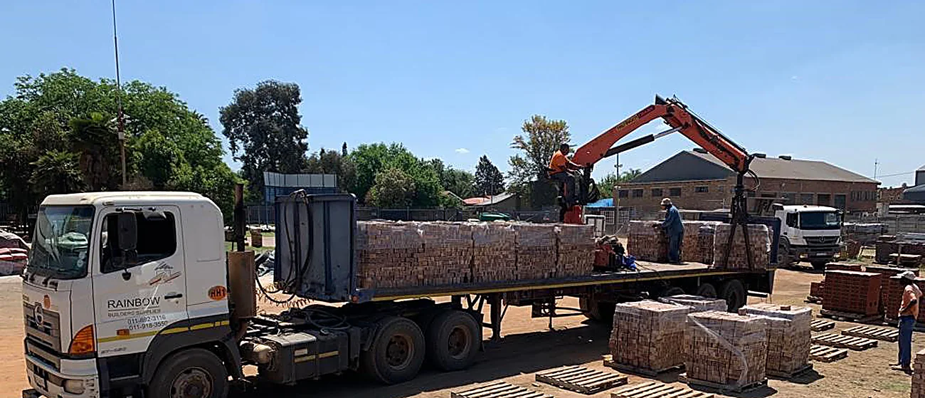 Rainbow flatbed truck being loaded with brick pallets by a crane arm