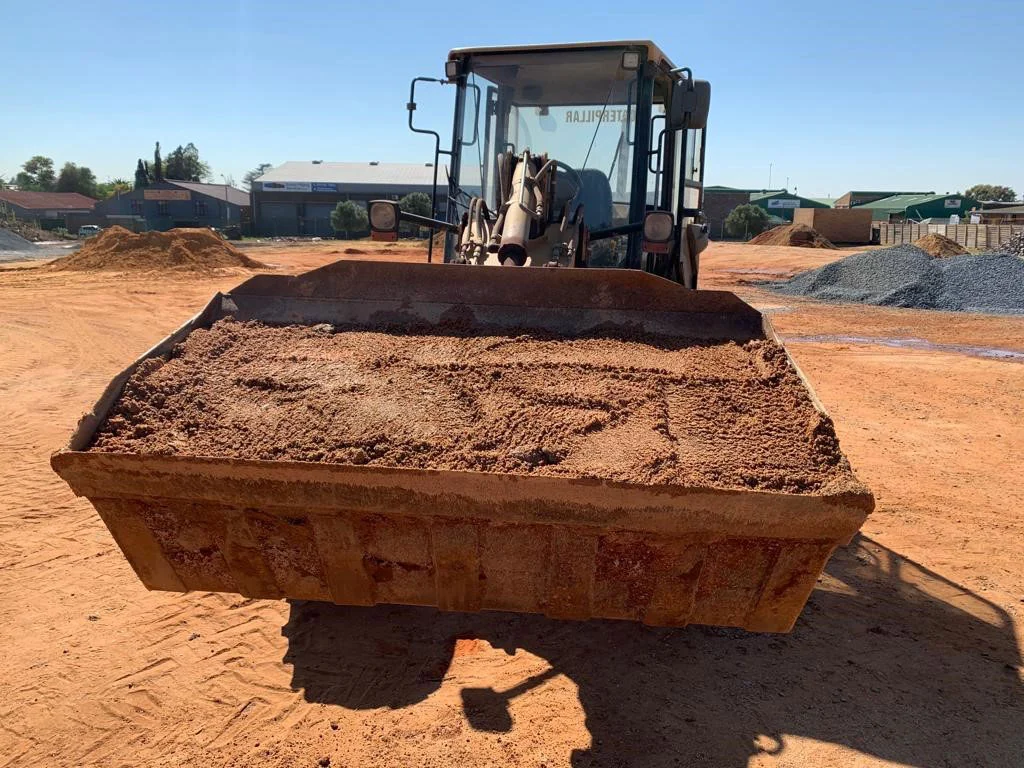 Front-end loader bucket filled with river sand, aggregate stockpiles behind